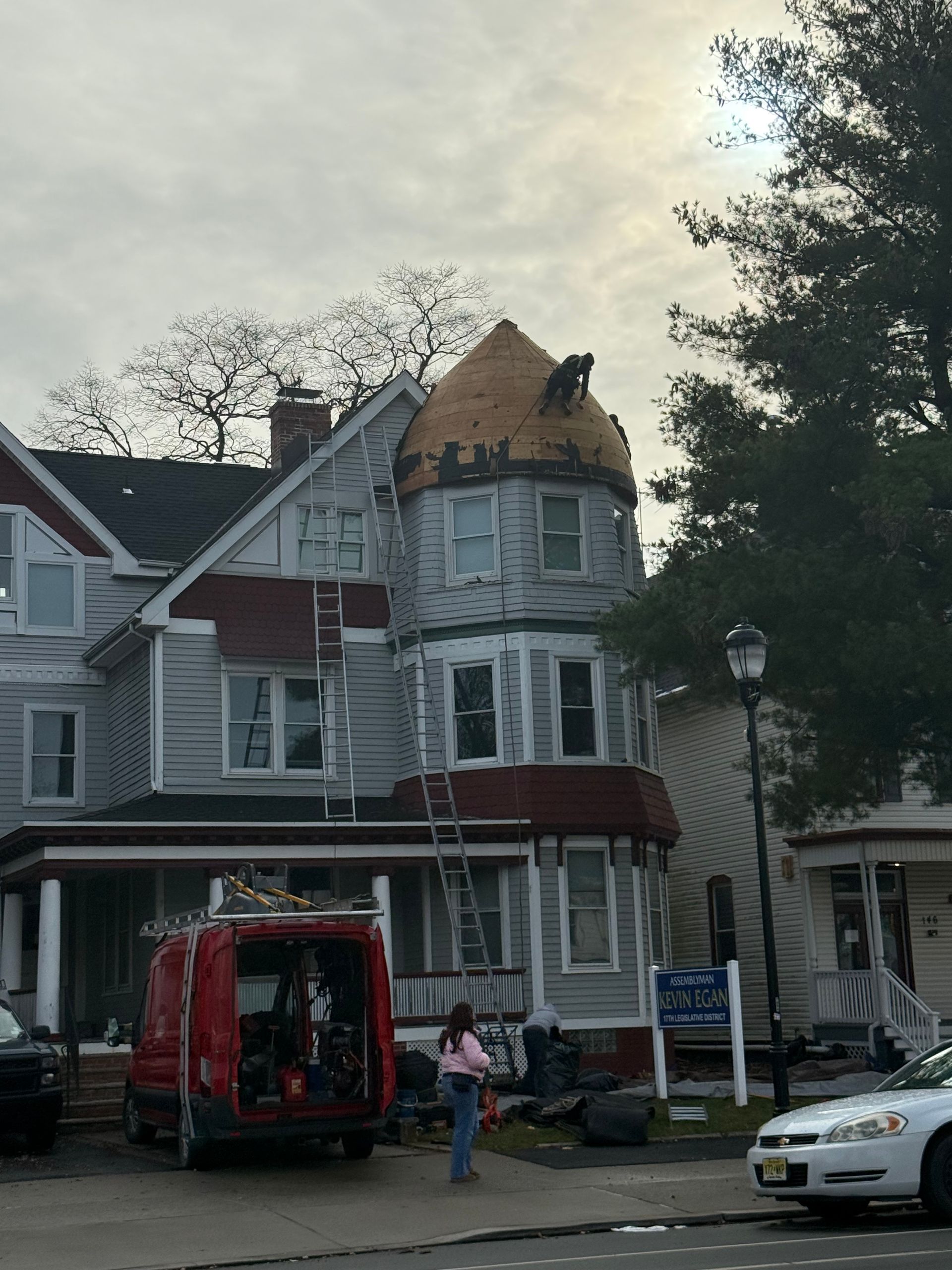 Victorian house with damaged roof, tree on the right, and people unloading from a red truck in front