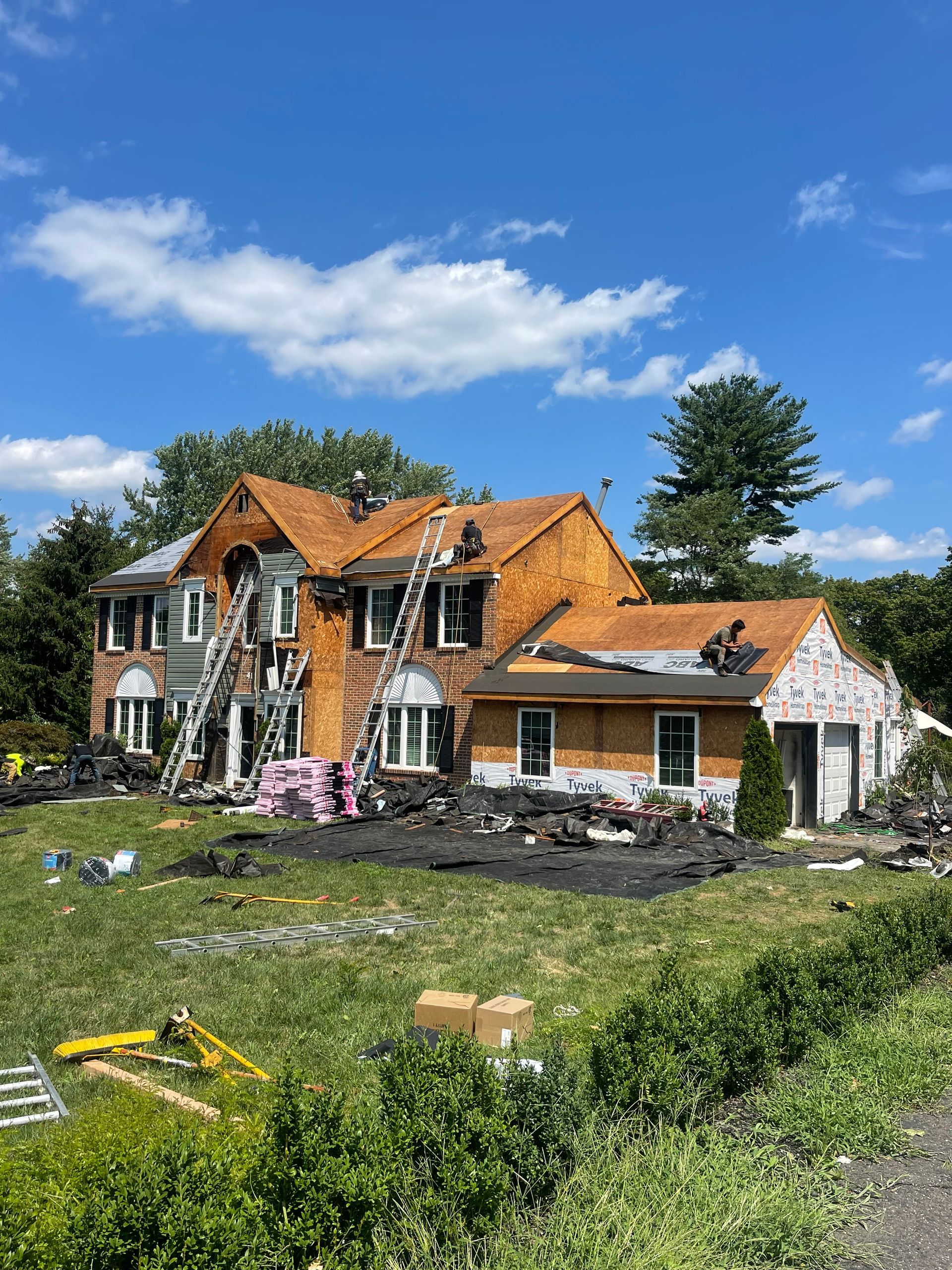 Damaged house with roof fire damage and debris in front yard under a blue sky