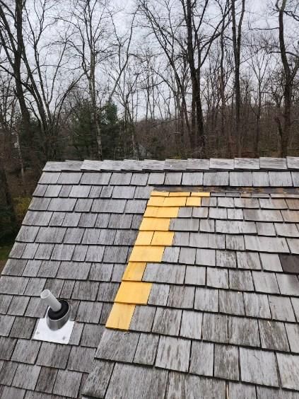 Damaged shingle roof with a yellow patch of replacement shingles and a vent pipe.