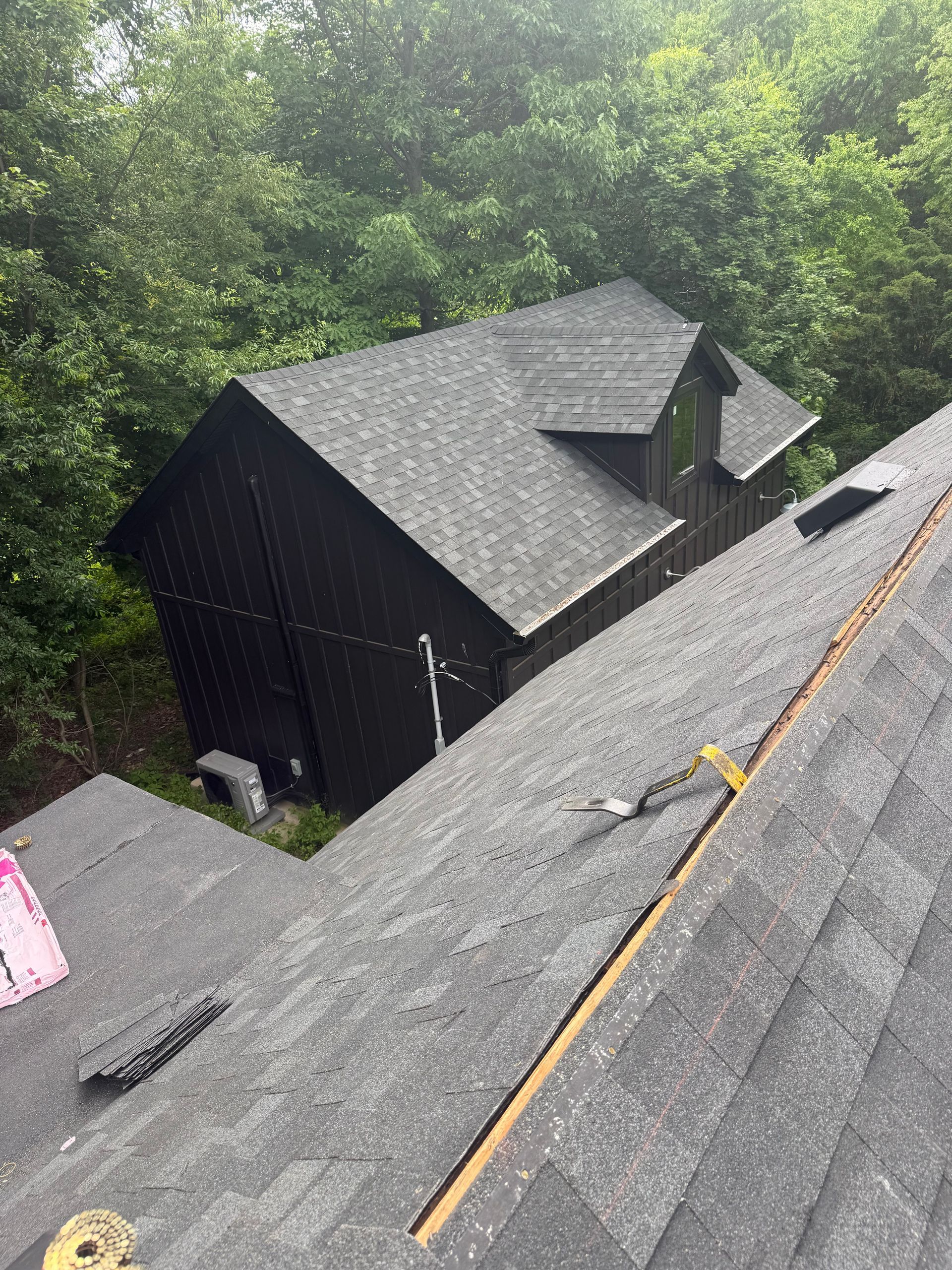Roof shingles under repair beside a wooded house, with a yellow measuring line across the roof.