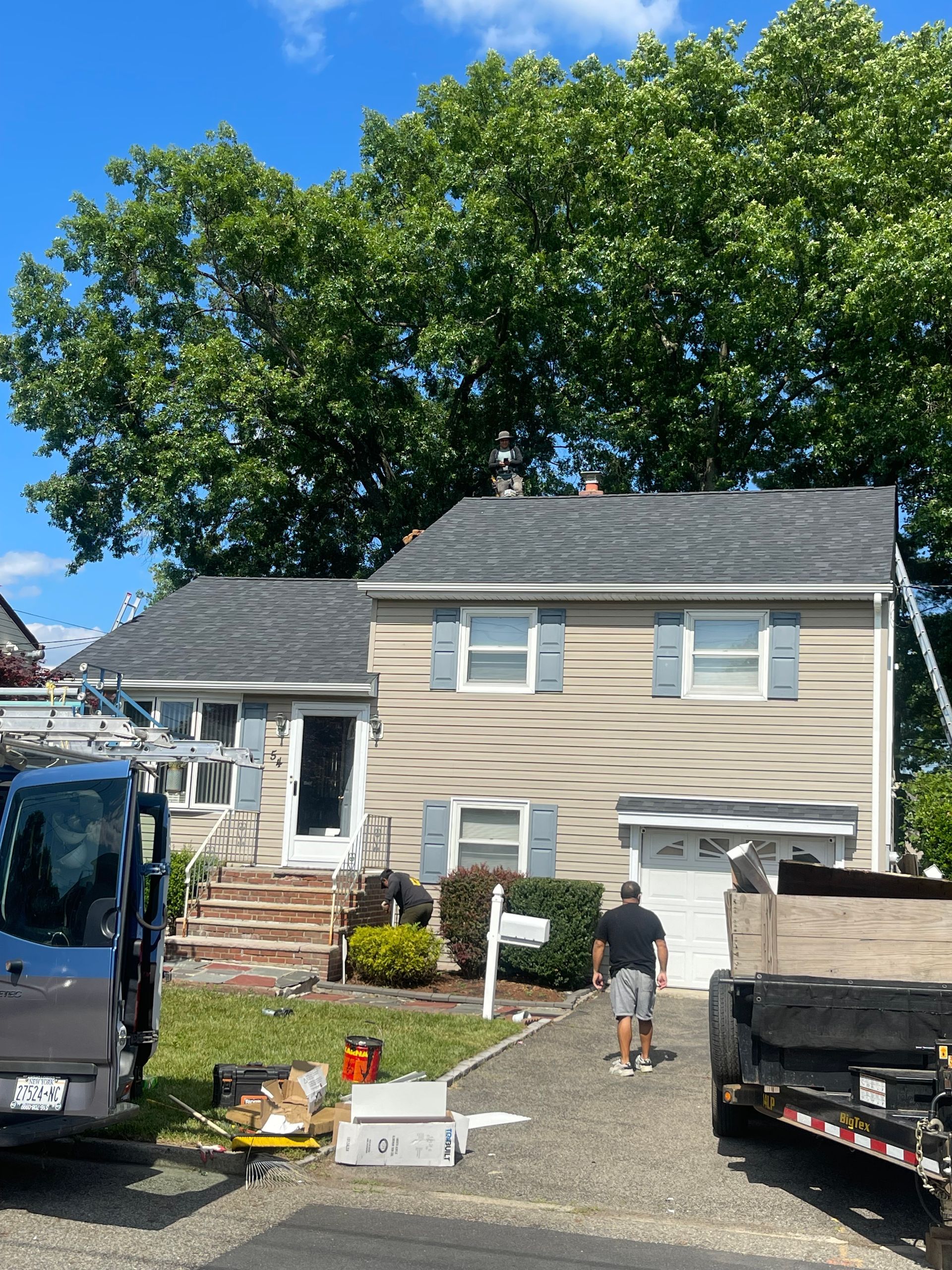 House under repair with workers, a van, and a dumpster in the driveway on a sunny day
