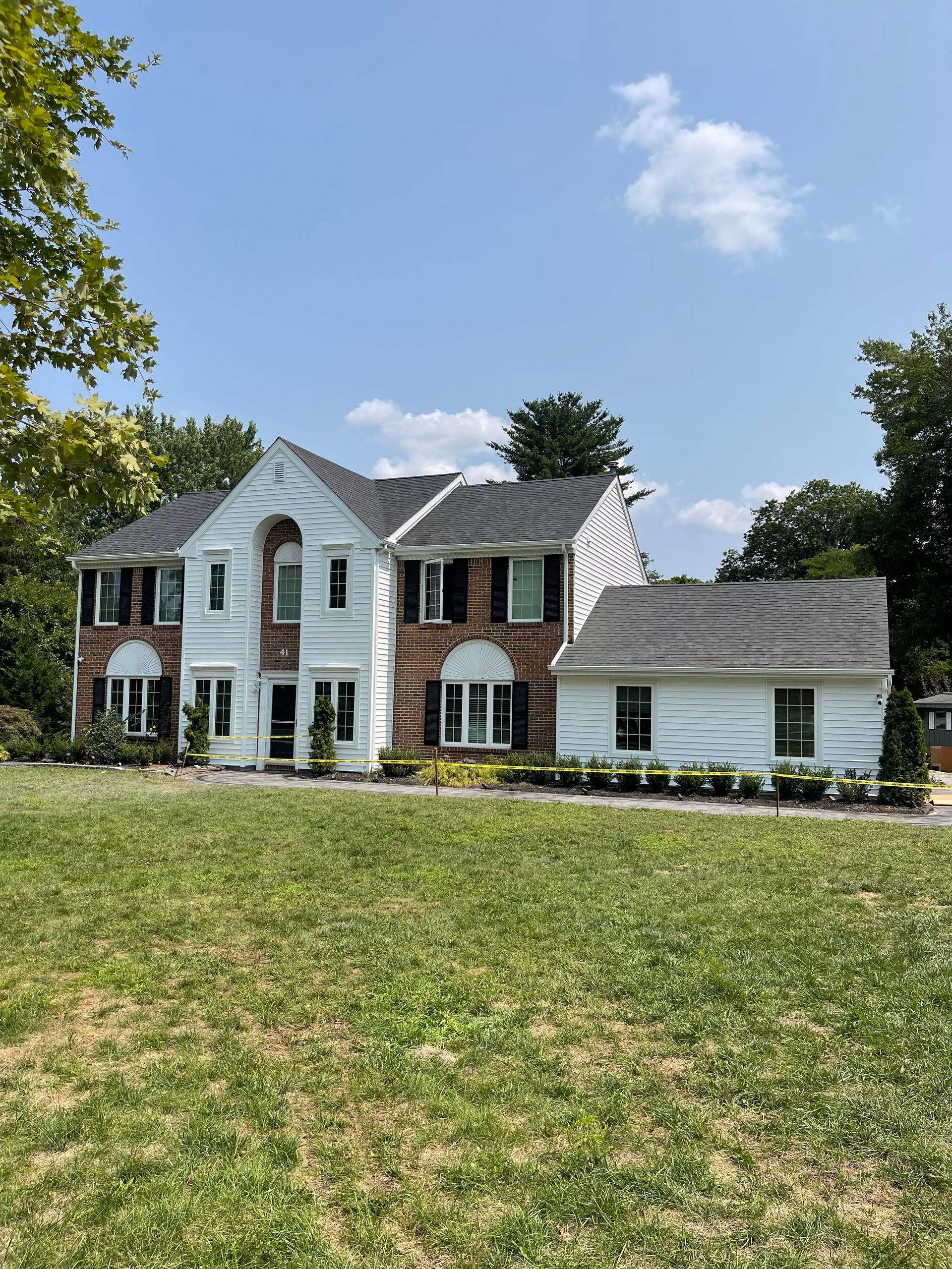 Large white colonial-style house with brick accents and a wide lawn under a blue sky