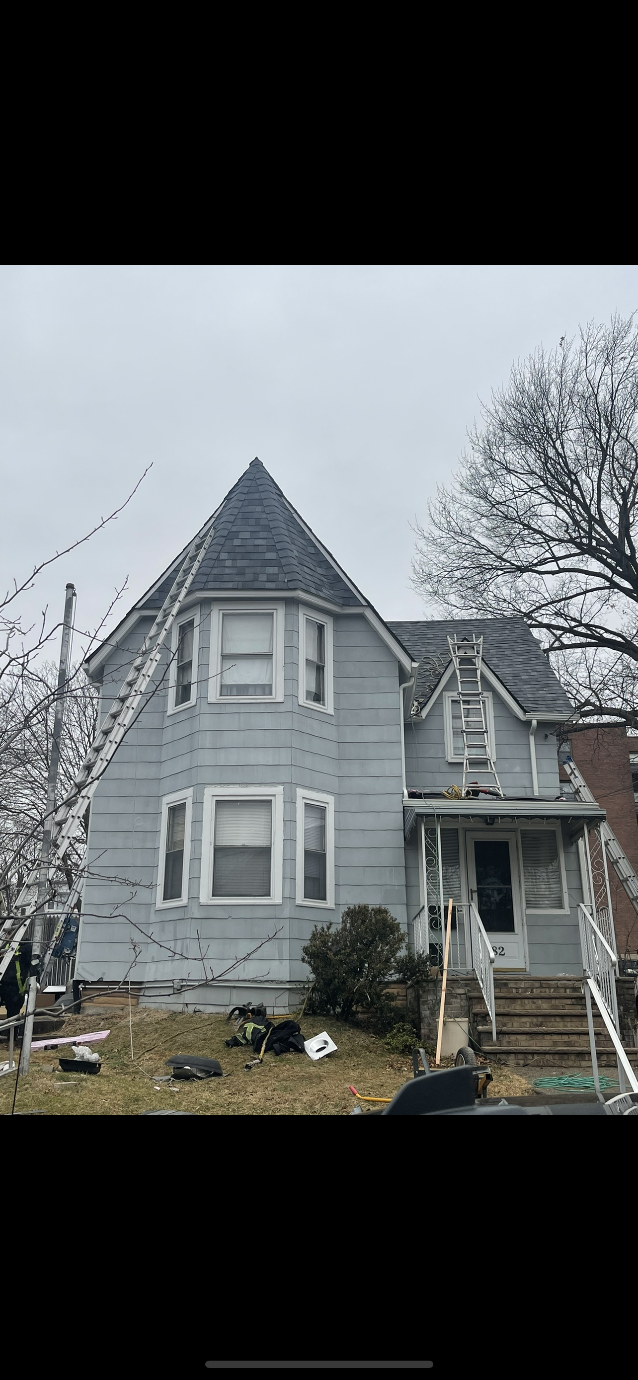 Gray two-story house with a turret and front porch, viewed from the yard on an overcast day