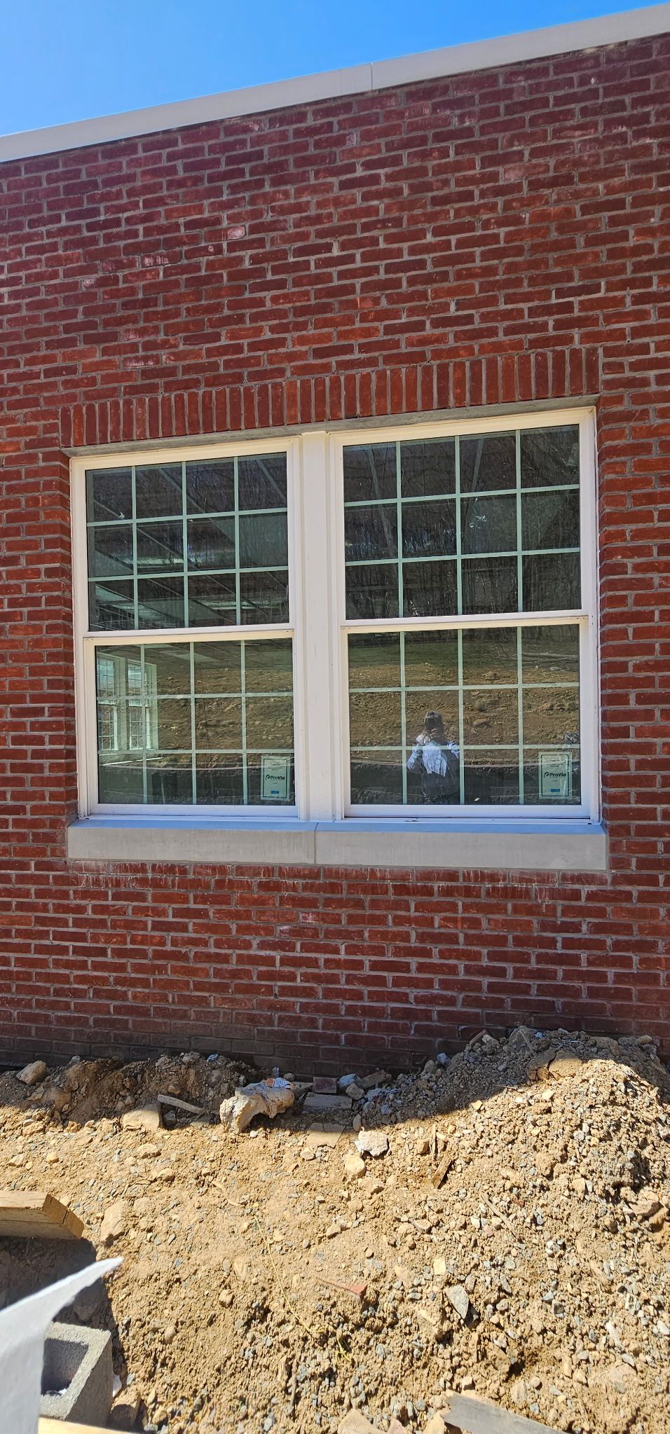 Brick wall with a white-framed window above a dirt bed