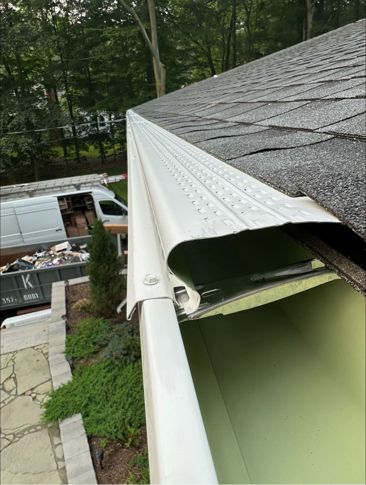Damaged white gutter and roof edge with exposed green soffit beside a house and truck below