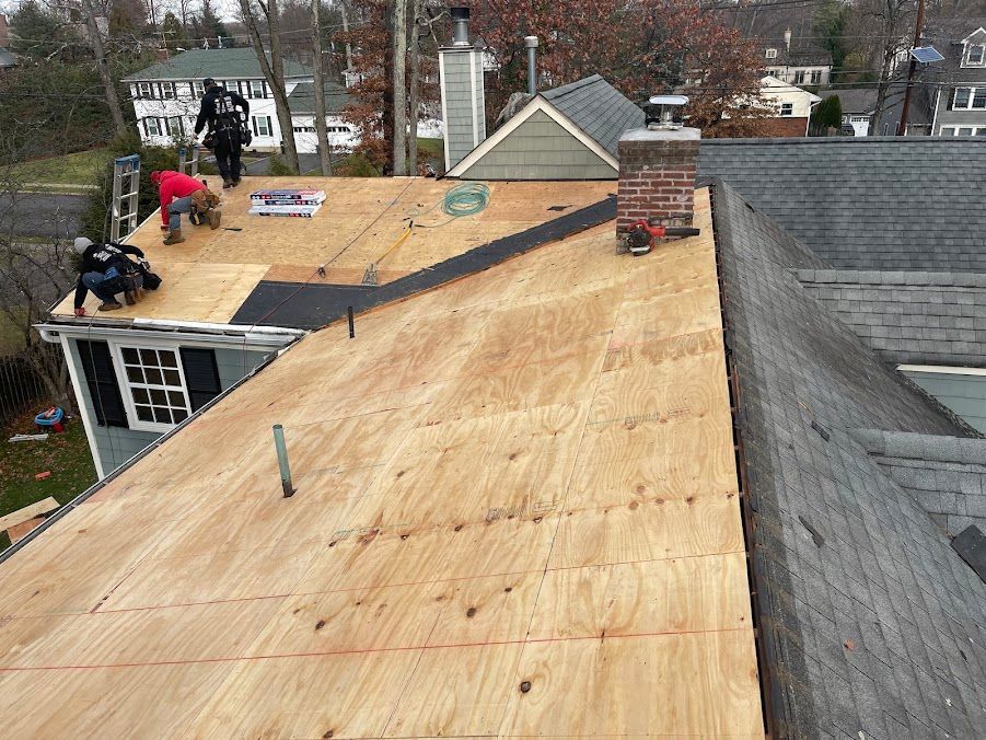 Roof under repair with plywood sheathing and two workers on a residential house