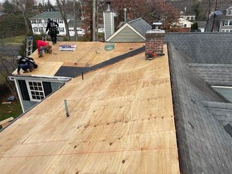 Roof under repair with plywood sheathing and two workers on a residential house