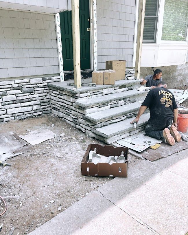 Worker stacking stone veneer beside a house entrance during exterior construction.