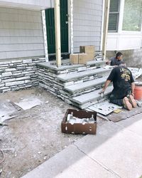 Worker stacking stone veneer beside a house entrance during exterior construction.