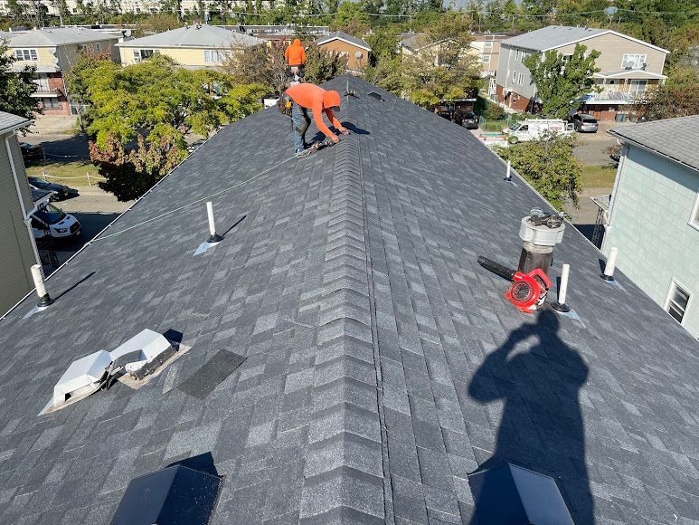 Roofing workers installing dark shingles on a house roof with tools and safety gear