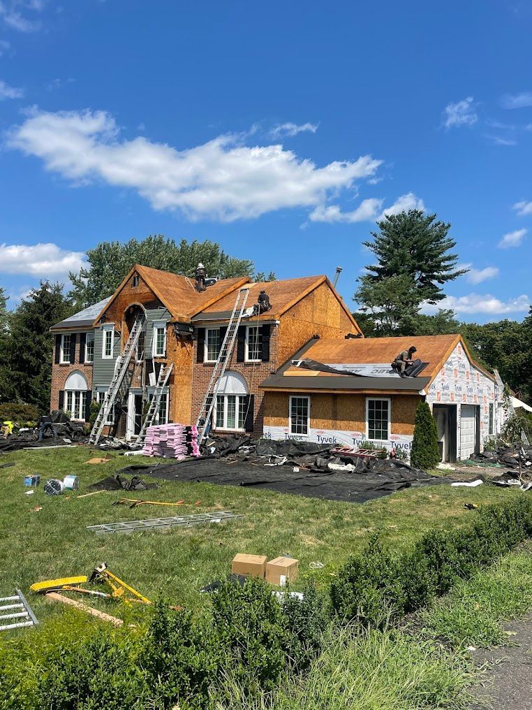 Damaged house with burned roof and debris in front, under a bright blue sky