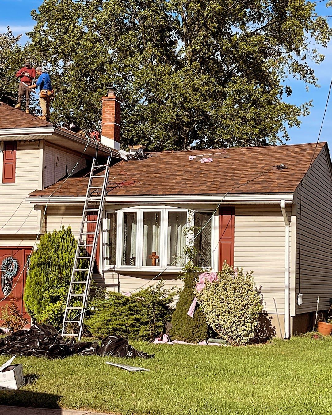 Worker on ladder repairing roof of a suburban house with damaged shingles.