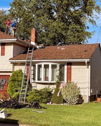 Worker on ladder repairing roof of a suburban house with damaged shingles.