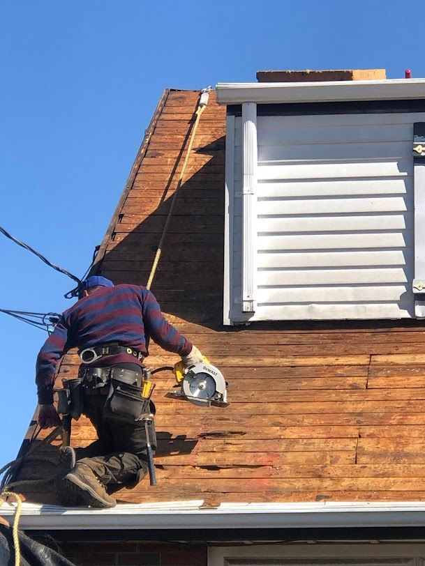 Worker on a roof using a circular saw near a dormer under a blue sky.