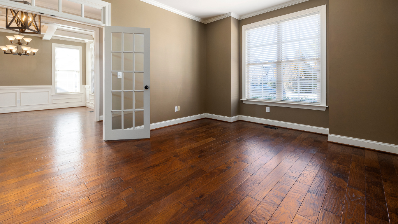An empty living room with hardwood floors and brown walls.