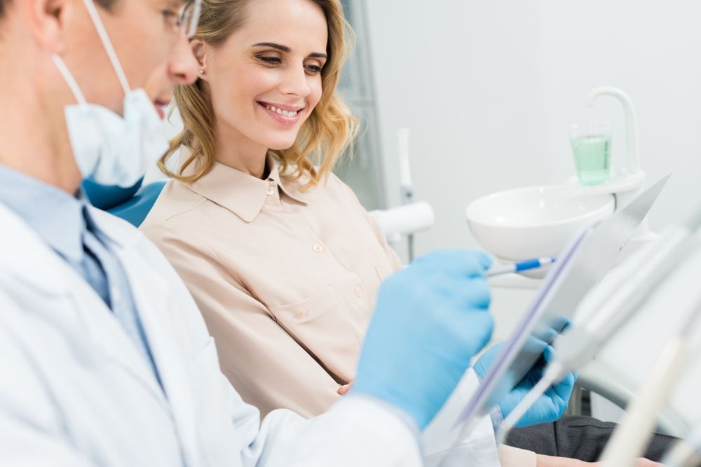 A Woman Is Sitting In A Dental Chair While A Dentist Looks At A Tablet — Mittagong Dental Care In Mittagong, NSW