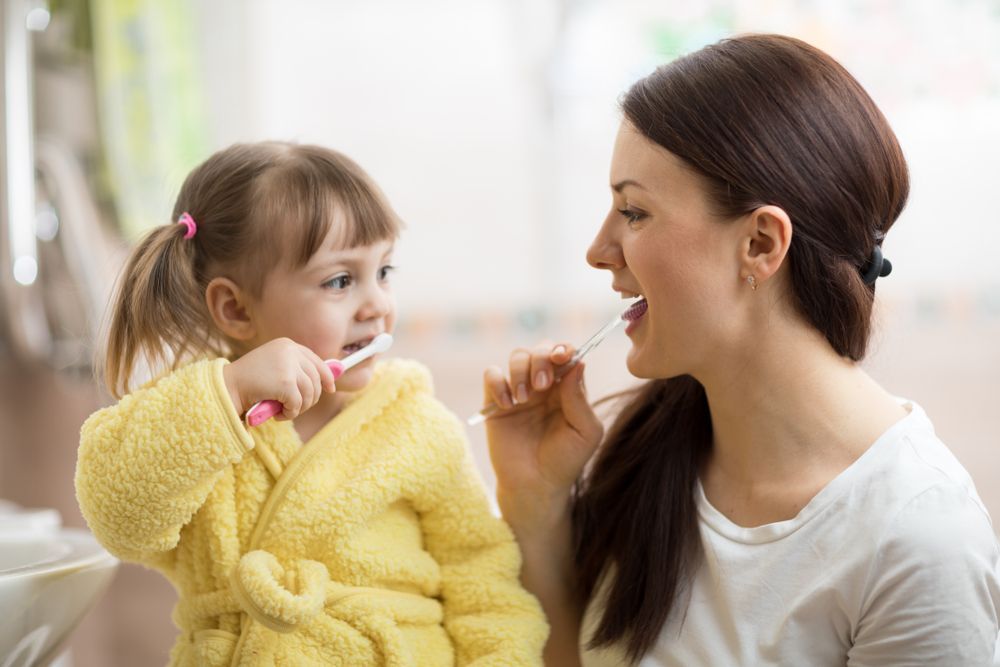 A Woman And A Little Girl Are Brushing Their Teeth Together — Mittagong Dental Care In Mittagong, NSW