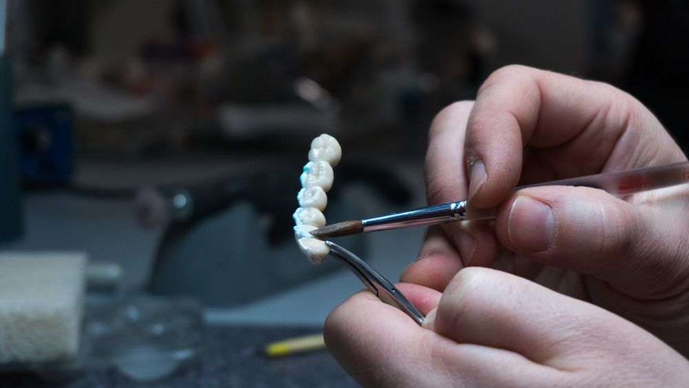 A Person Is Working On A Dental Bridge With A Brush And Tweezers — Mittagong Dental Care In Mittagong, NSW