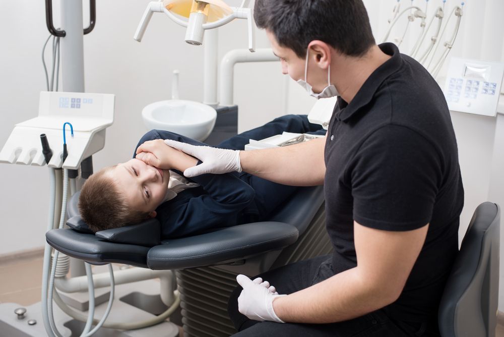A Young Boy Is Laying In A Dental Chair While A Dentist Examines His Teeth — Mittagong Dental Care In Mittagong, NSW