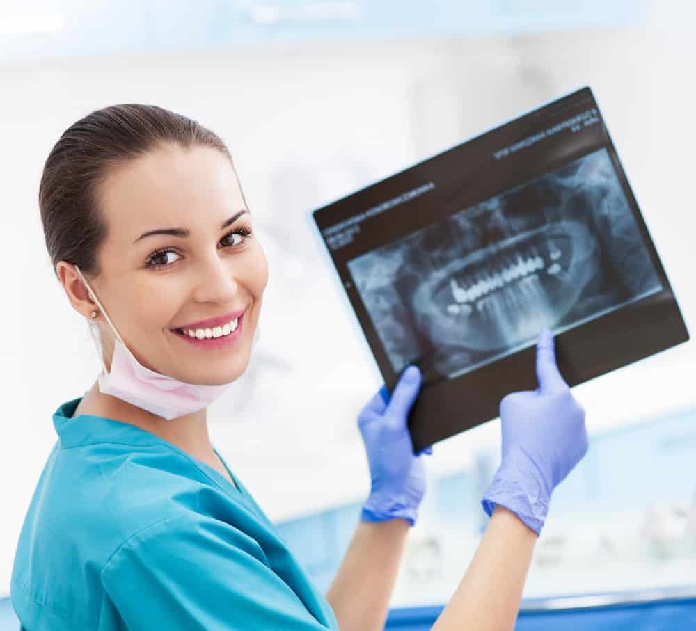 A Female Dentist Is Smiling While Holding An X-ray Of Her Teeth — Mittagong Dental Care In Mittagong, NSW
