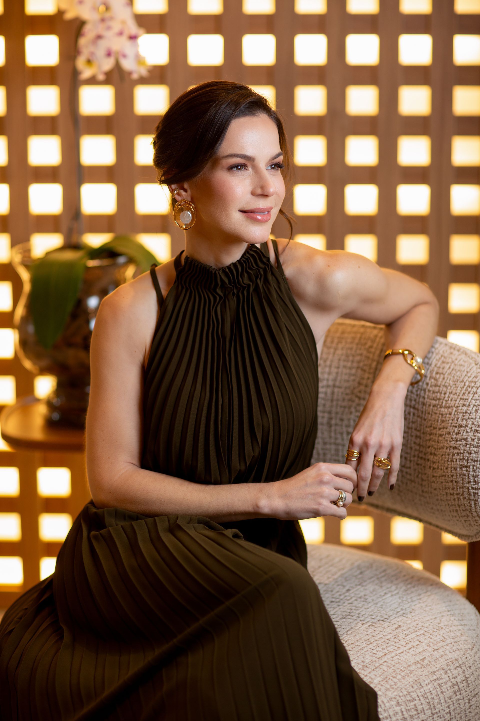 Uma mulher está sentada em uma mesa com as mãos cruzadas e sorrindo.