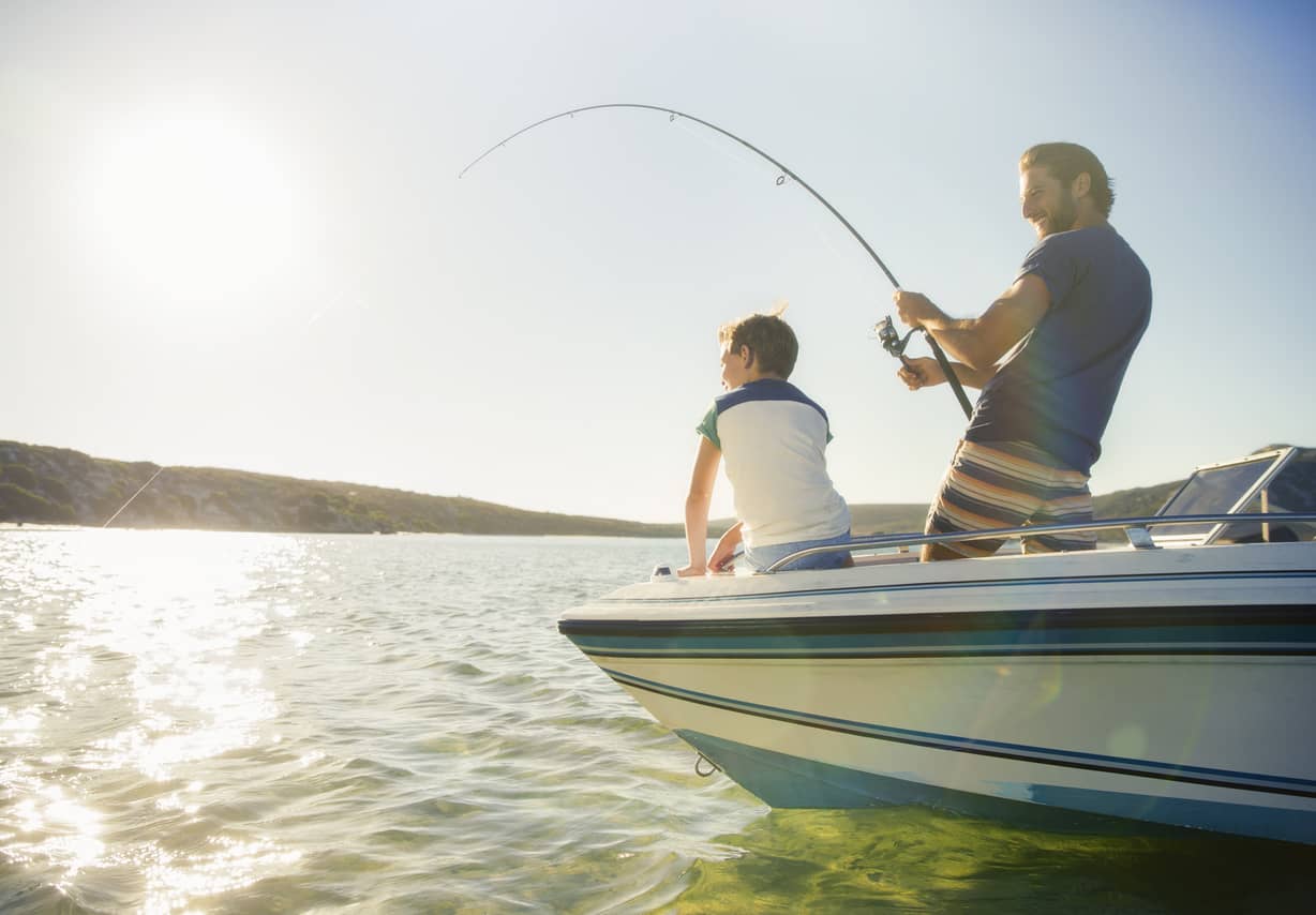 Two people fishing from a boat on a sunny lake, with one person holding a bent fishing rod