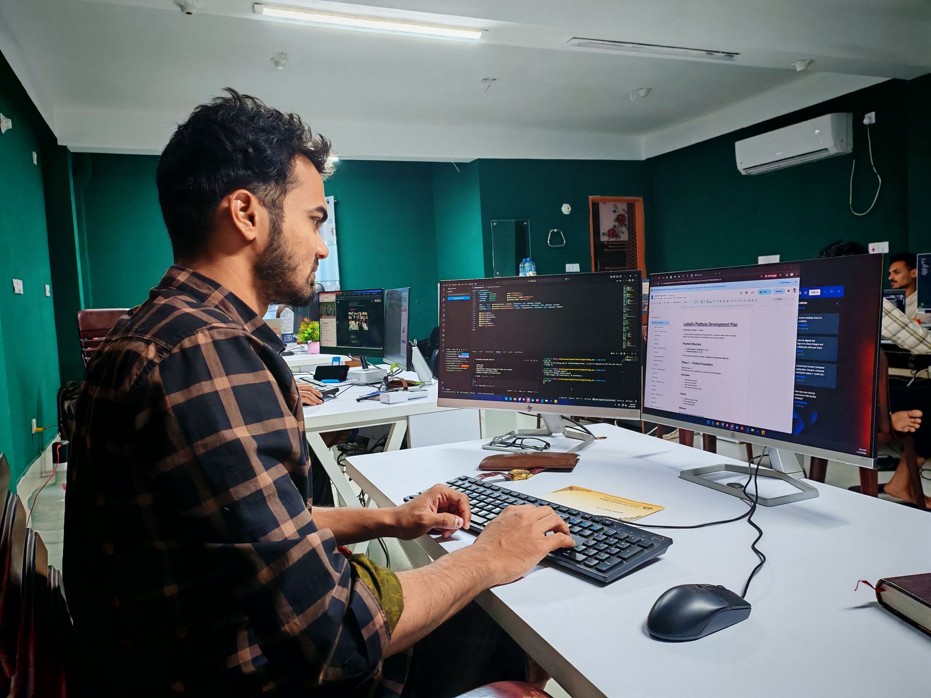 Man working at a desk with multiple monitors in a modern office, typing on a keyboard.