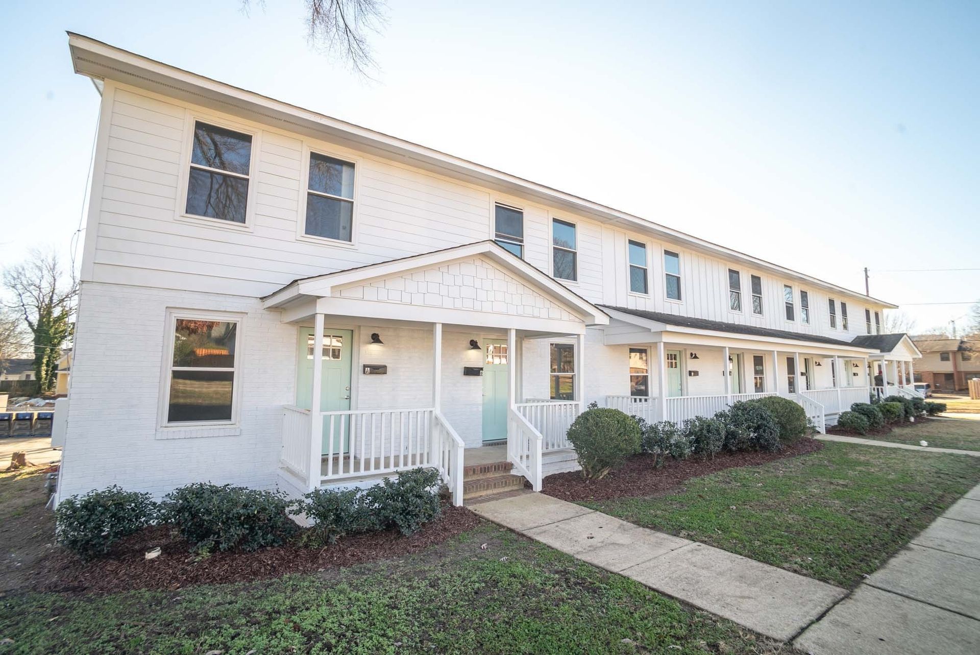 A white brick building with a porch and a sidewalk in front of it.