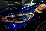 Hand polishing the headlight and hood of a dark blue car with a cloth and yellow-blue wristbands