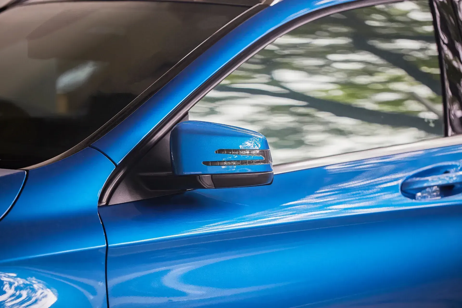 Blue car door and side mirror with trees reflected in the window