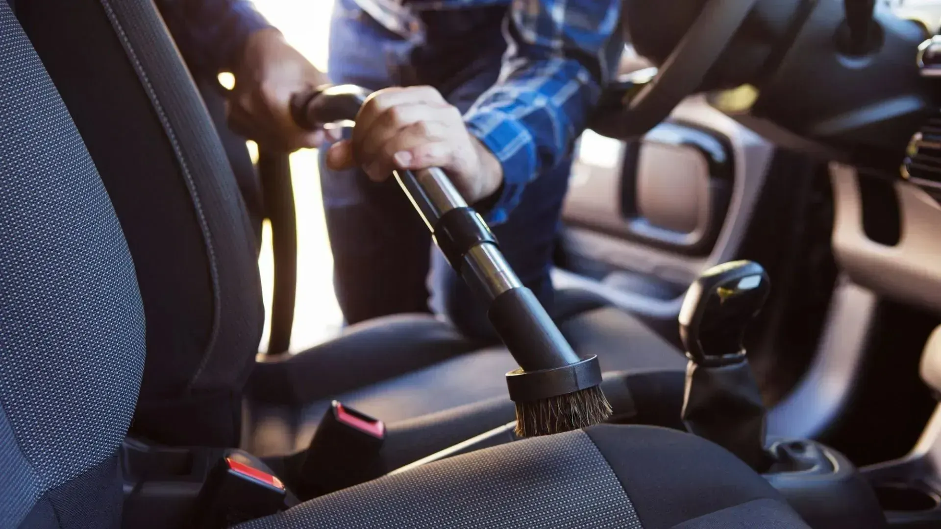Person vacuuming a car seat with a handheld attachment inside a vehicle interior