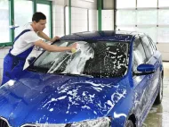 Man washing a blue car with soapy water at a car wash.