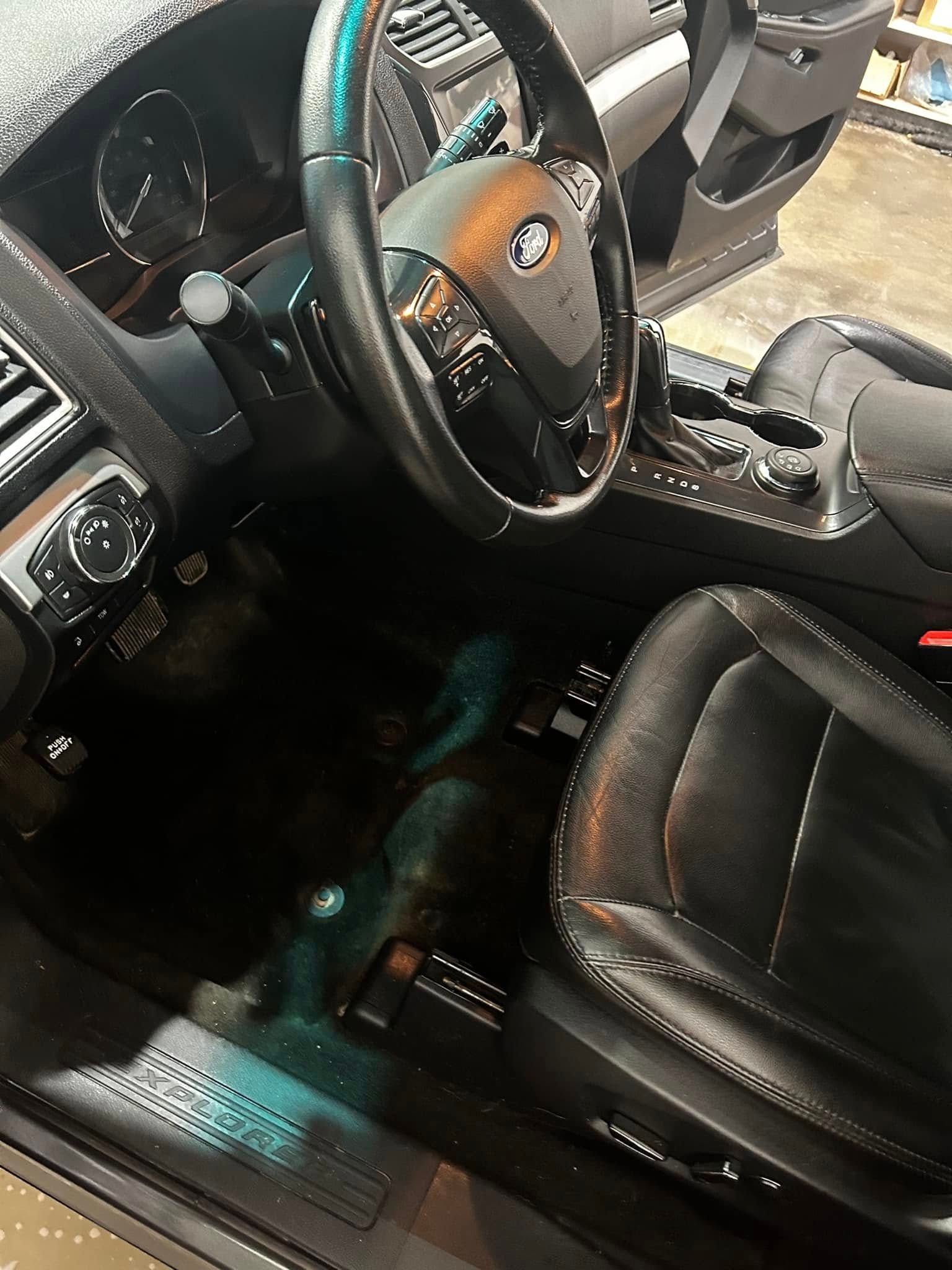Black leather car interior with steering wheel, center console, and driver’s seat lit by sunlight