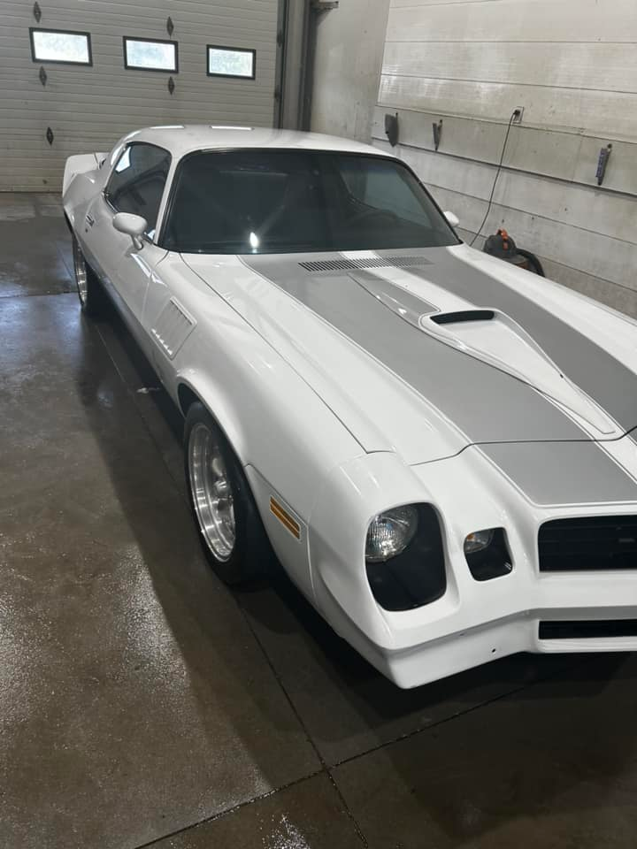 White classic muscle car with gray racing stripes parked in a wet garage