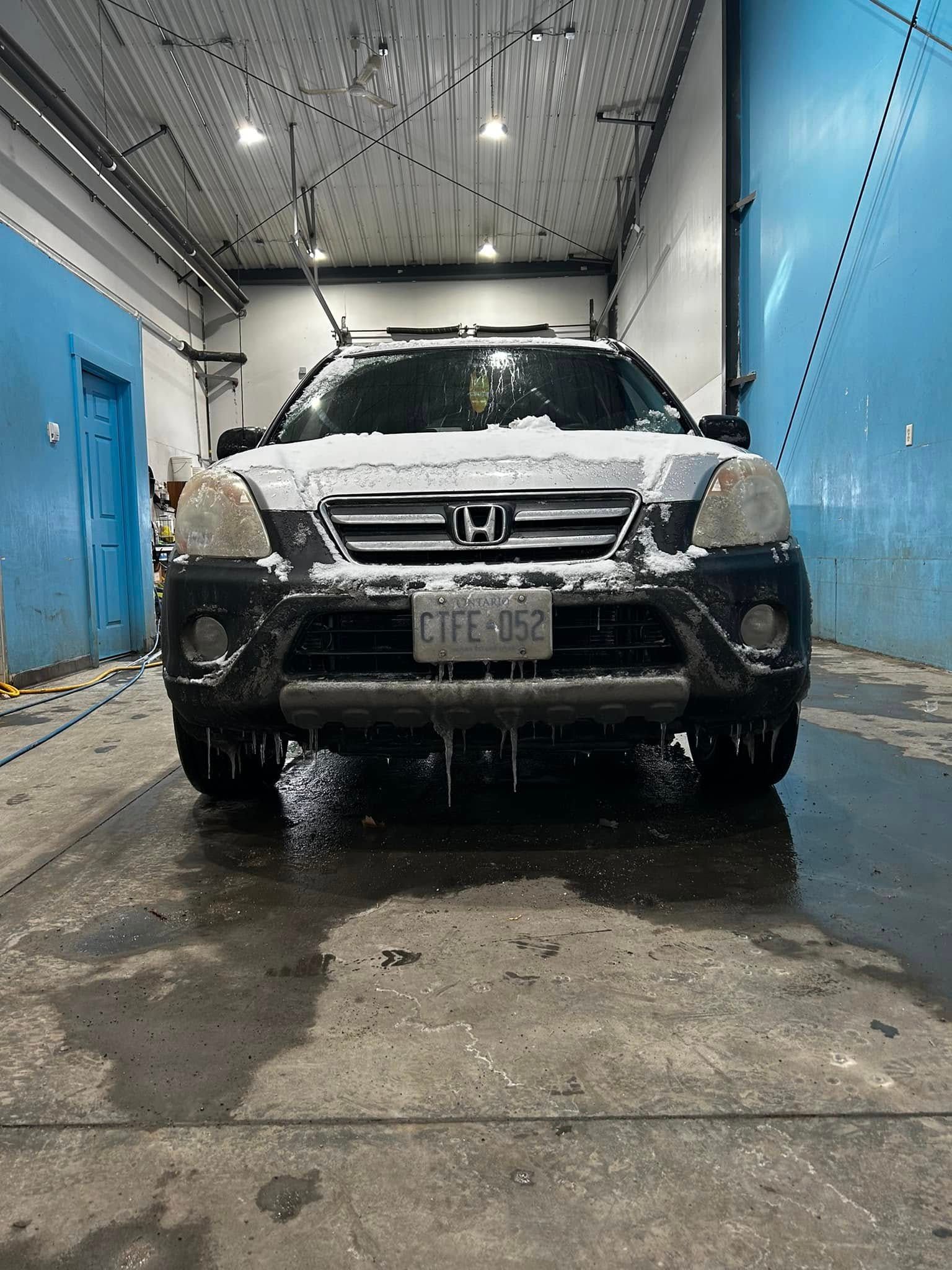 Honda SUV in a car wash bay, covered in soap and water.