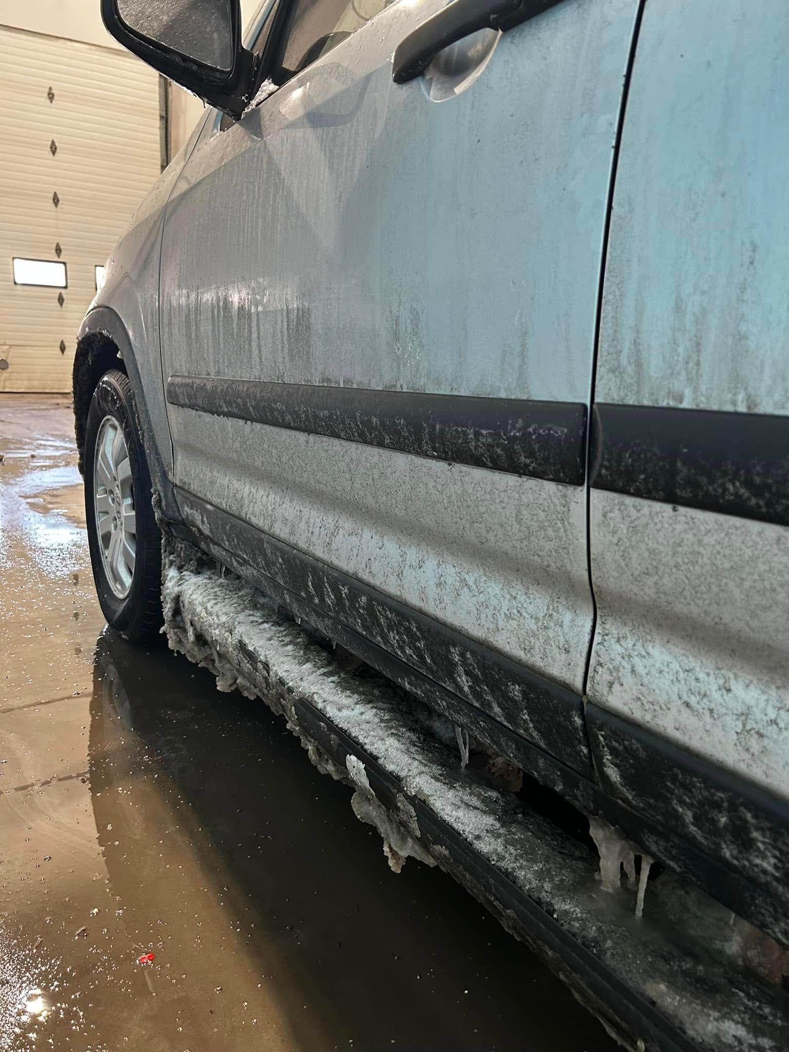 Blue car covered in slushy ice, parked in a wet car wash bay