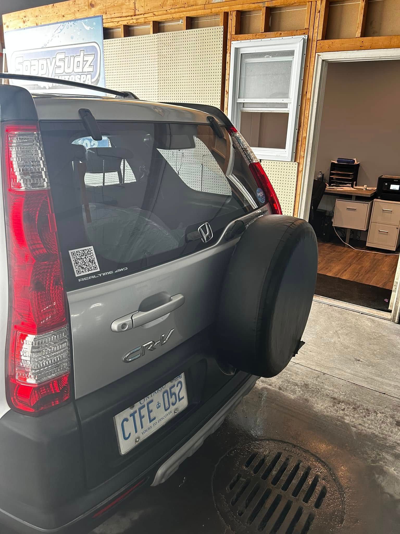 Dark SUV parked in a garage, viewed from the rear with a spare tire mounted on the back.