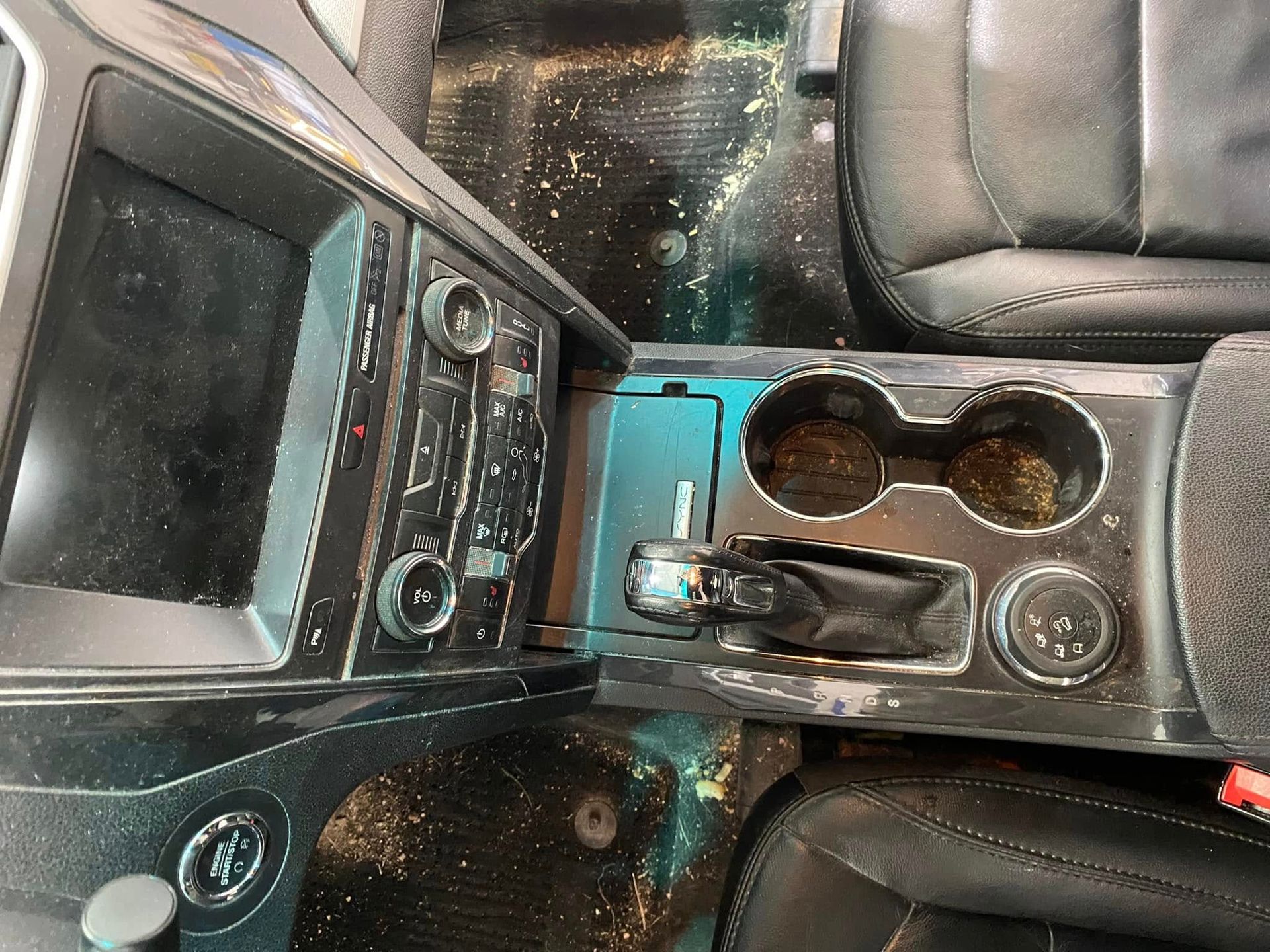 Car center console with touchscreen, cup holders, and black leather seats with water spots
