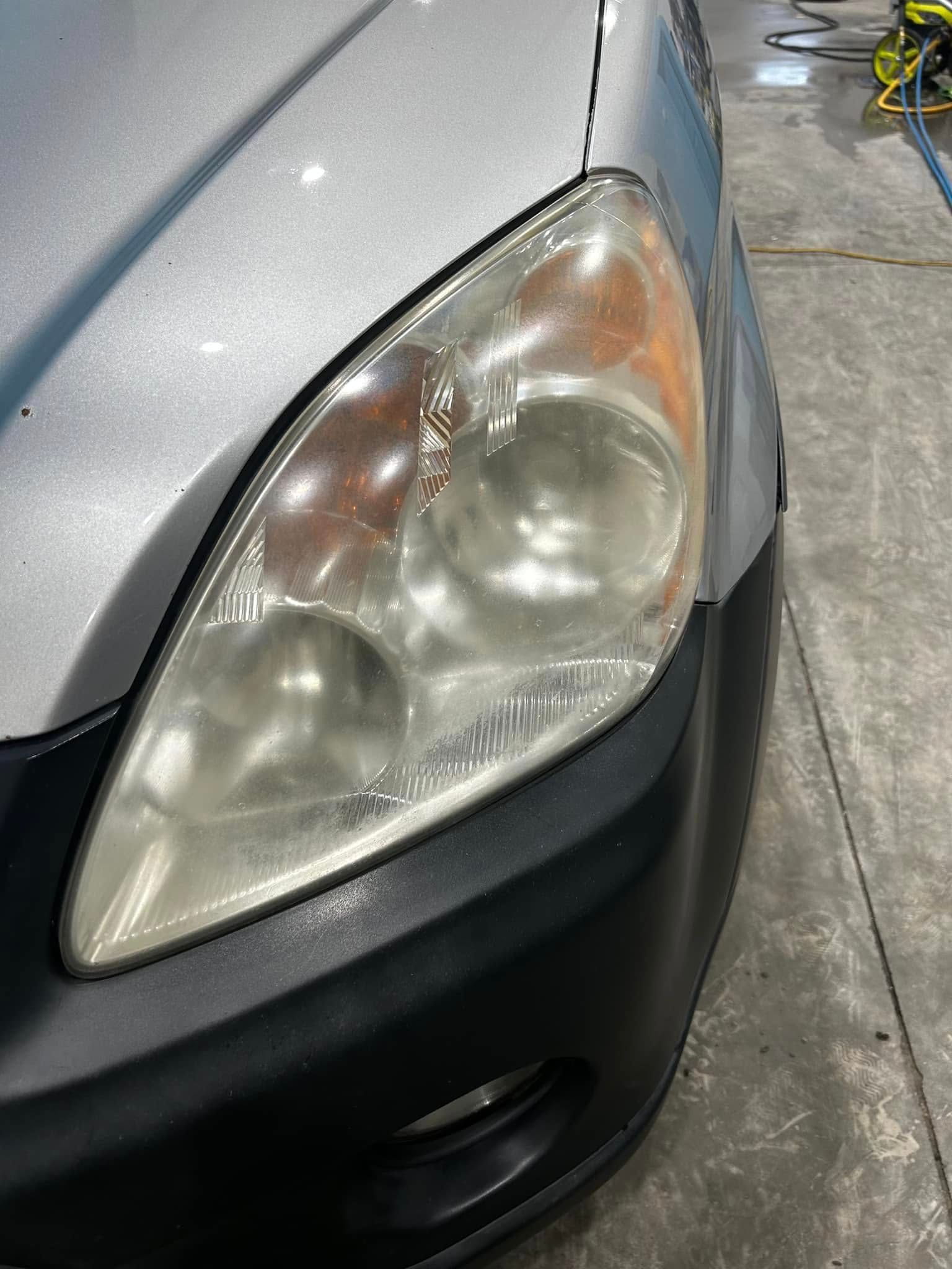Close-up of a silver car’s front headlight and bumper on a garage floor.