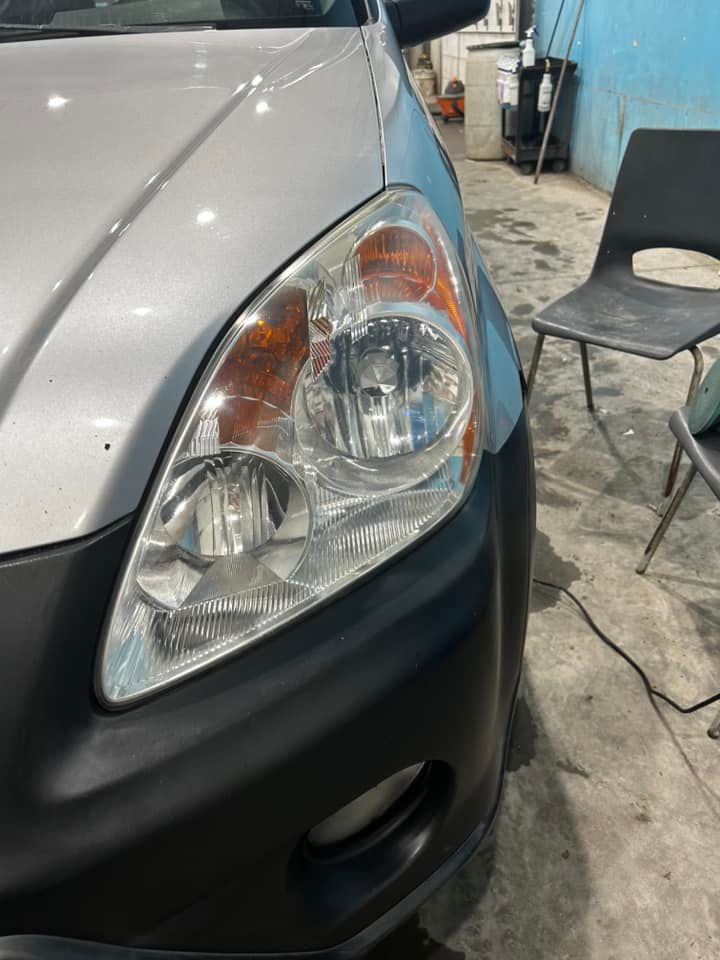 Front corner of a silver car with a blue fender and black bumper in a garage.