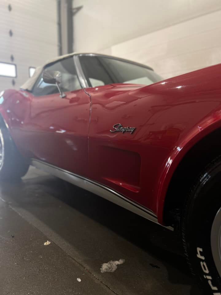 Red Corvette Stingray side view in a garage, with glossy red paint and chrome trim.