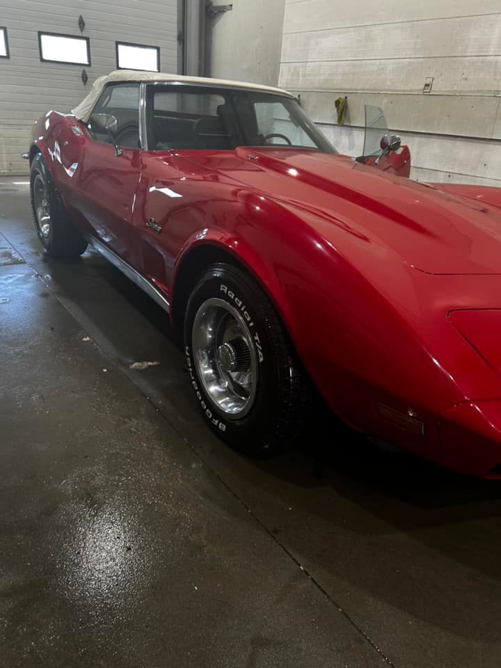 Red classic sports car parked indoors in a garage, viewed from the front side.