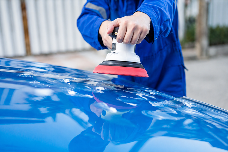 Person polishing a blue car with a buffer in a workshop