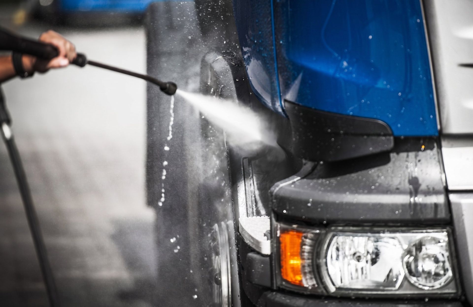 Pressure washing the front of a blue truck with a spray nozzle