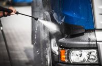 Pressure washing the front of a blue truck with a spray nozzle