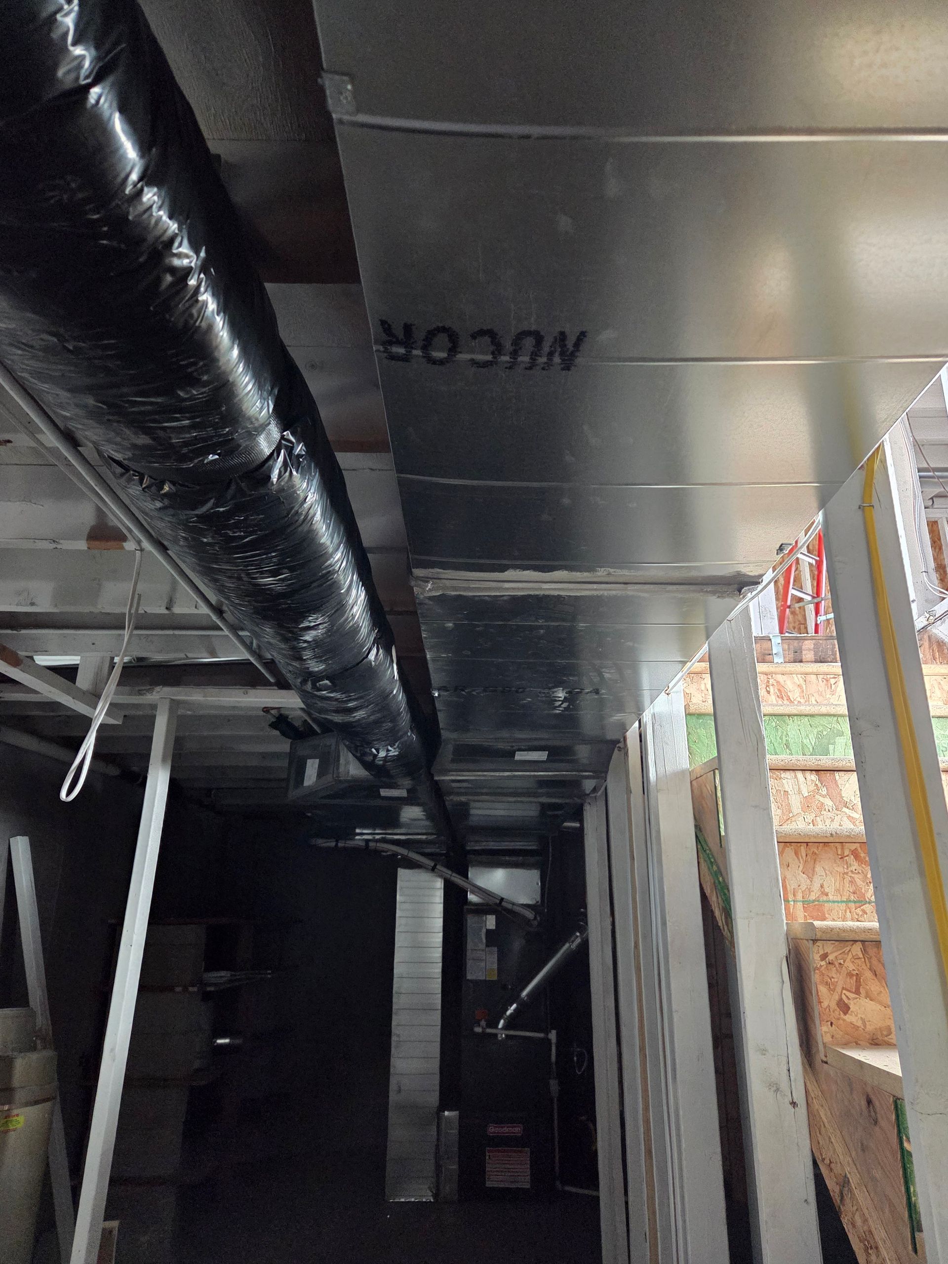 HVAC ductwork and insulated flex duct in a basement ceiling, with a staircase on the right.
