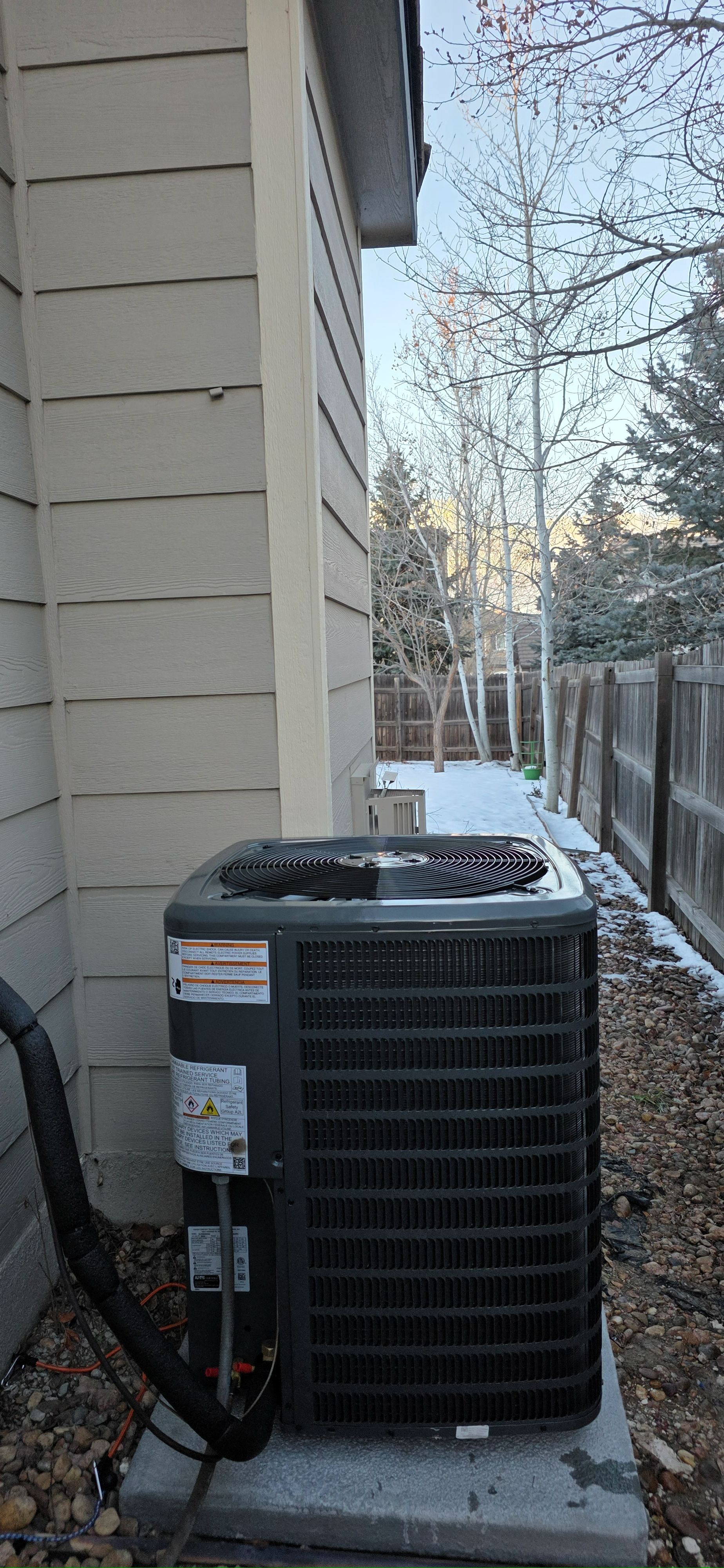 An outdoor HVAC unit next to a house, winter landscape in background.