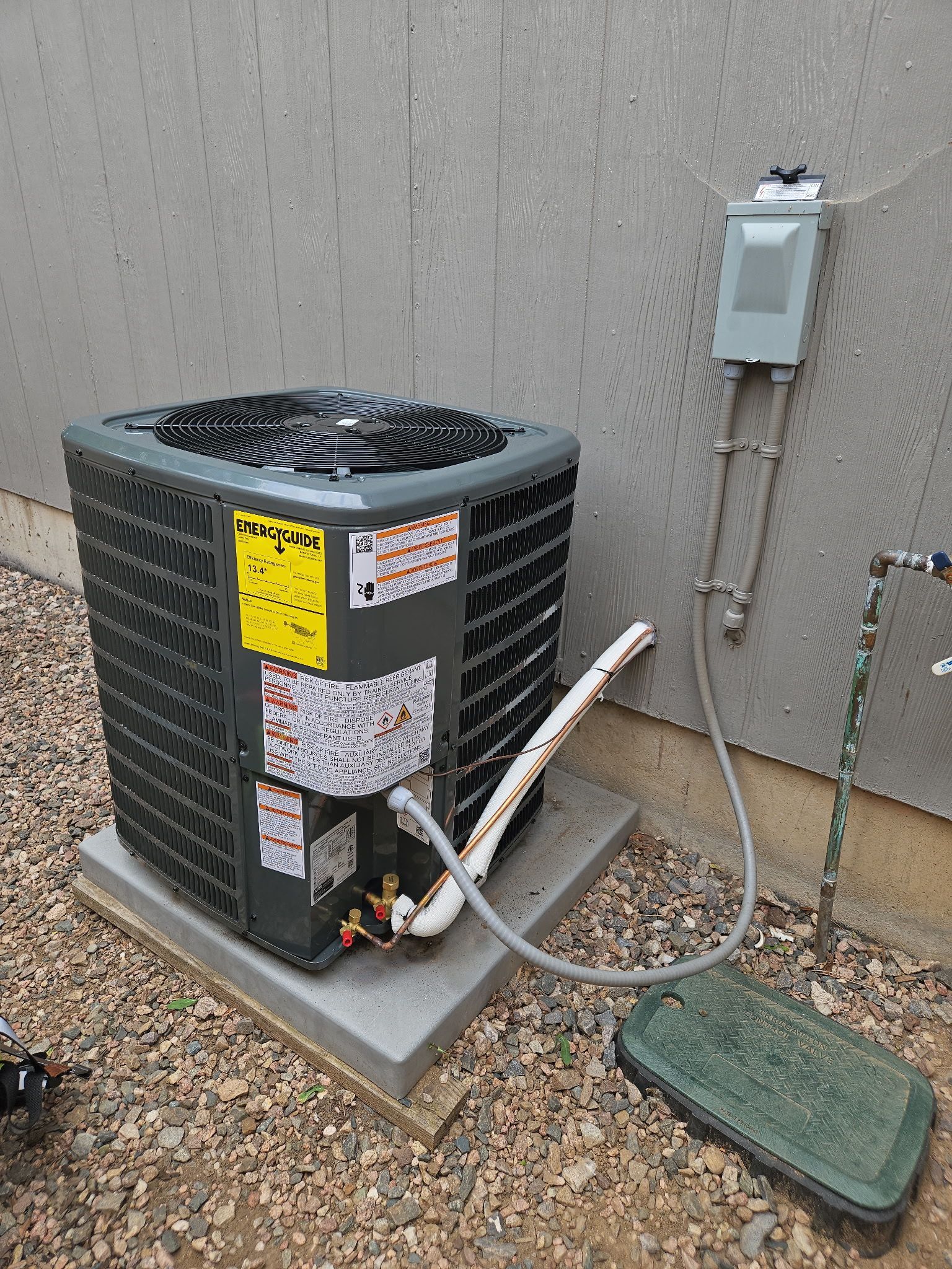 Air conditioning unit outside a building, on a concrete pad. Electrical box and conduit visible.