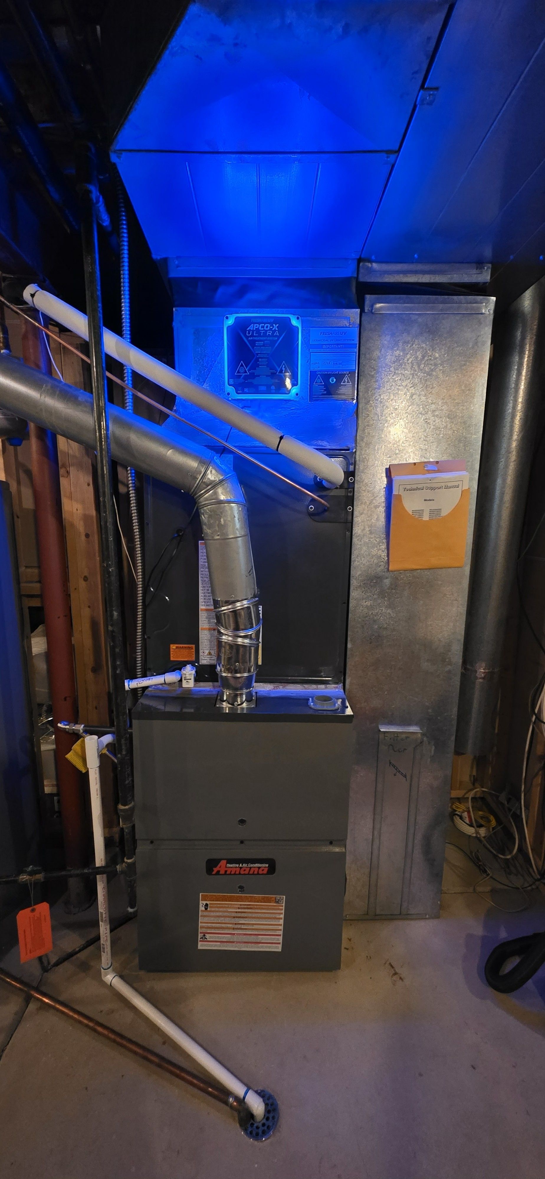 Furnace in a basement. Ductwork and blue overhead lighting are visible.