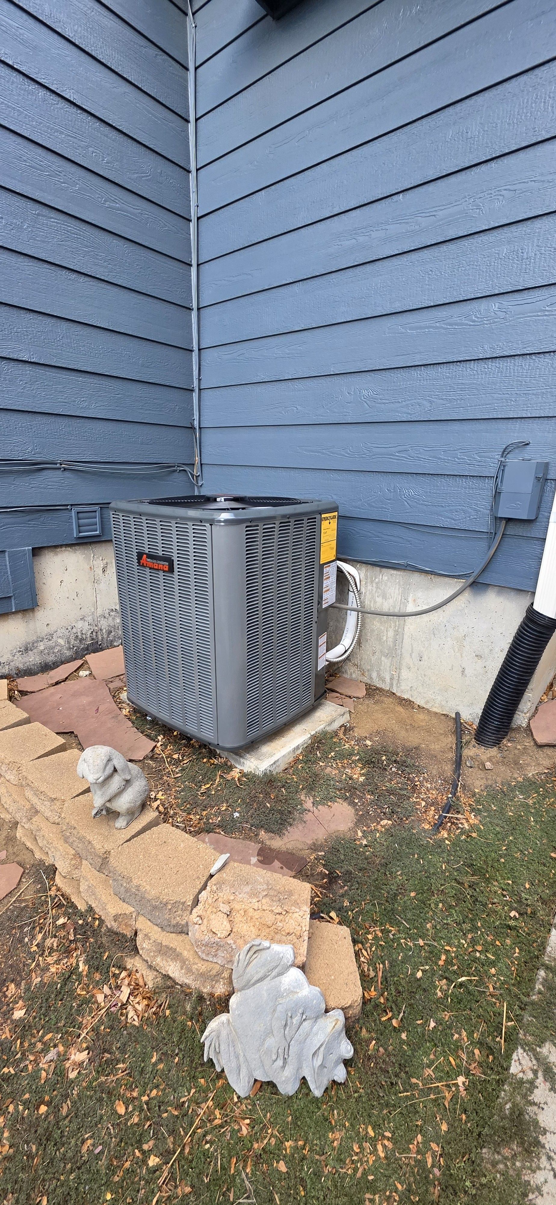 An air conditioning unit next to a blue house with decorative stone and grass.
